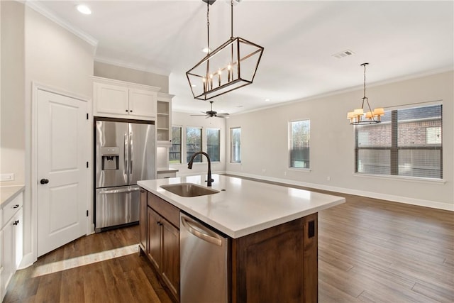 kitchen with ceiling fan with notable chandelier, stainless steel appliances, sink, a center island with sink, and white cabinetry