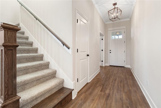 foyer entrance with dark wood-type flooring, ornamental molding, and a notable chandelier