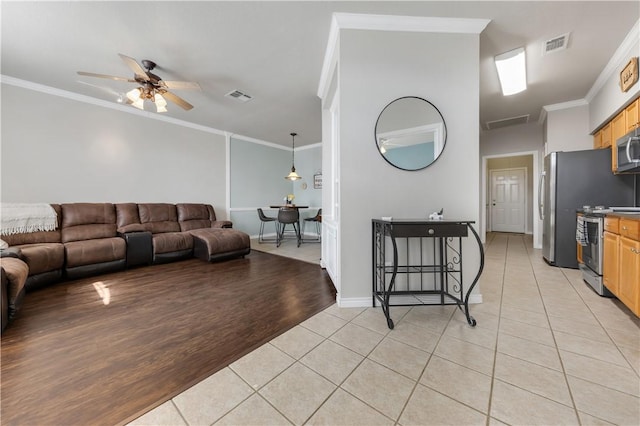 living room featuring light tile patterned floors, visible vents, a ceiling fan, and ornamental molding