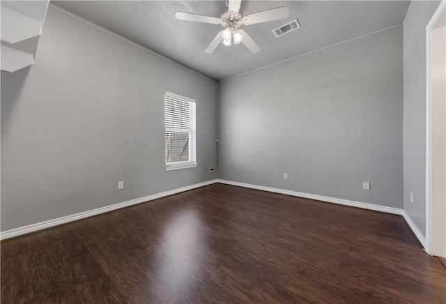 empty room featuring dark wood finished floors, visible vents, a ceiling fan, and baseboards