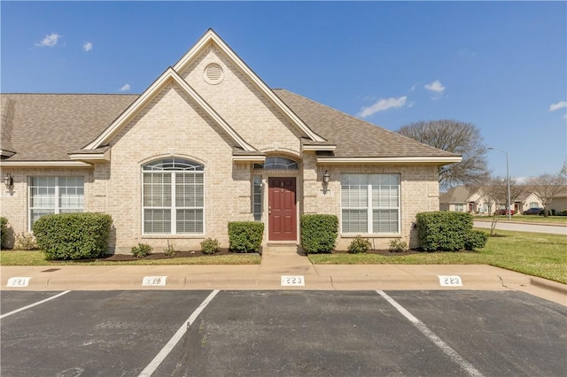 view of front of home with uncovered parking, brick siding, and roof with shingles