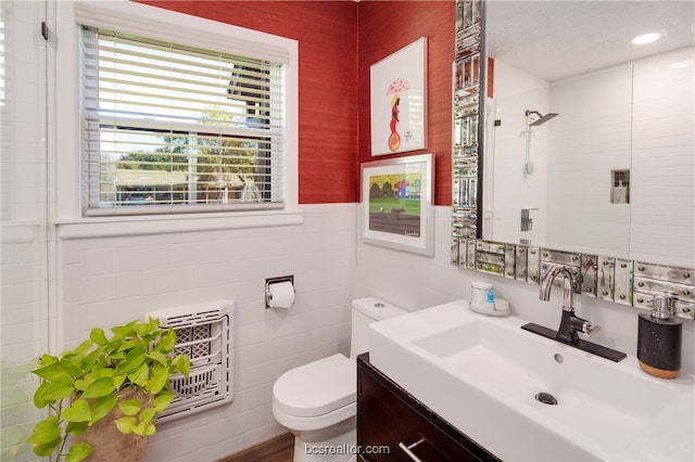 bathroom with heating unit, a shower, tile walls, vanity, and toilet