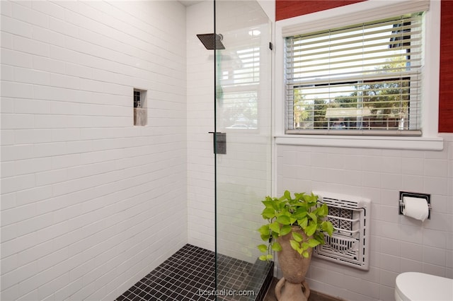 bathroom with tiled shower, toilet, heating unit, and tile walls