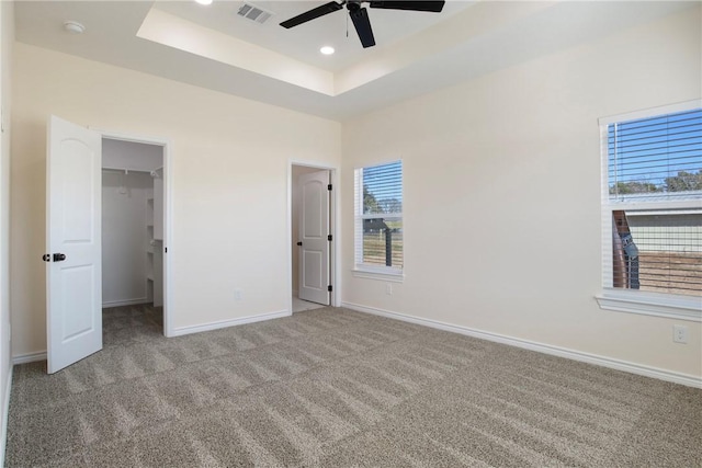 unfurnished bedroom featuring a walk in closet, light colored carpet, a raised ceiling, a closet, and ceiling fan