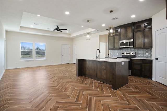 kitchen featuring sink, appliances with stainless steel finishes, dark parquet floors, pendant lighting, and a kitchen island with sink