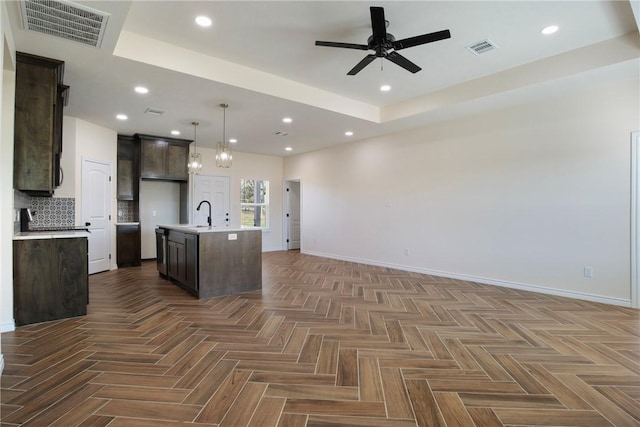 kitchen featuring pendant lighting, dark brown cabinets, a center island with sink, and dark parquet floors