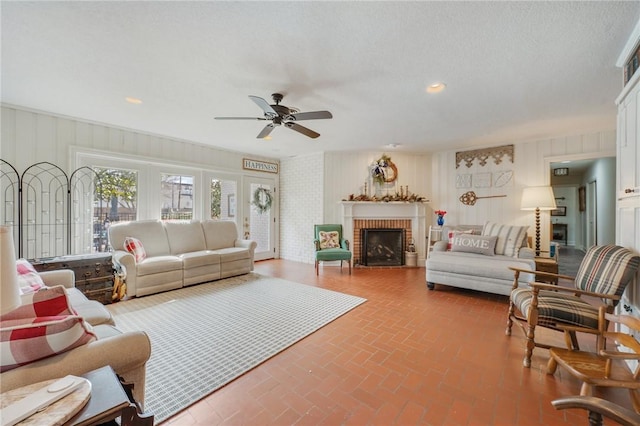 living room featuring ceiling fan, a textured ceiling, and a fireplace