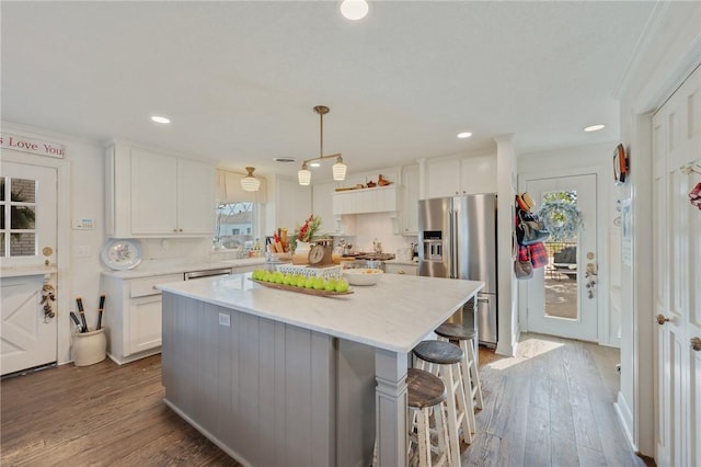 kitchen featuring dark wood-type flooring, appliances with stainless steel finishes, white cabinetry, a center island, and decorative light fixtures