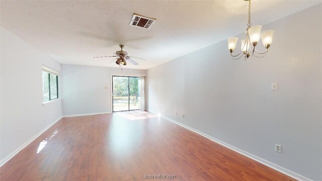 empty room with visible vents, baseboards, wood finished floors, and ceiling fan with notable chandelier