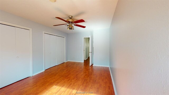 unfurnished bedroom with light wood-style flooring, baseboards, multiple closets, and a ceiling fan