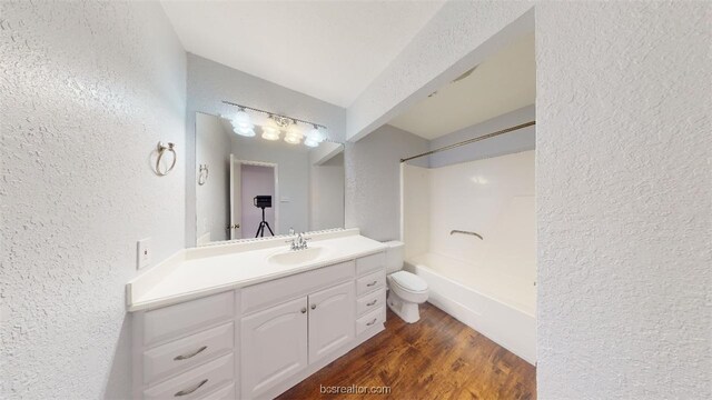 bathroom with shower / bathtub combination, vanity, toilet, wood finished floors, and a textured wall