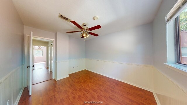 unfurnished room featuring wood finished floors, ceiling fan, visible vents, and plenty of natural light