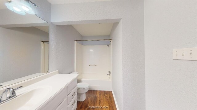 full bathroom with toilet, a textured wall,  shower combination, vanity, and wood finished floors