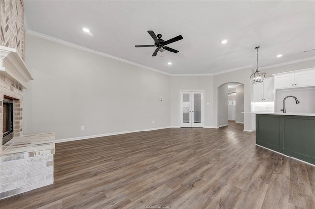 unfurnished living room with ceiling fan, crown molding, dark wood-type flooring, and a brick fireplace