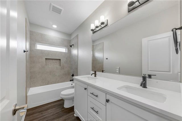 full bathroom featuring hardwood / wood-style floors, vanity, tiled shower / bath combo, and toilet