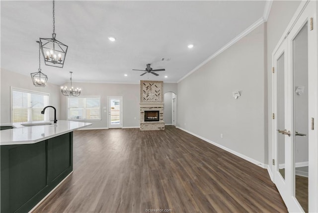 unfurnished living room featuring ceiling fan, sink, dark hardwood / wood-style flooring, crown molding, and a fireplace