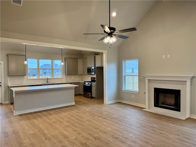 kitchen with gray cabinetry, ceiling fan, a center island, a fireplace, and appliances with stainless steel finishes