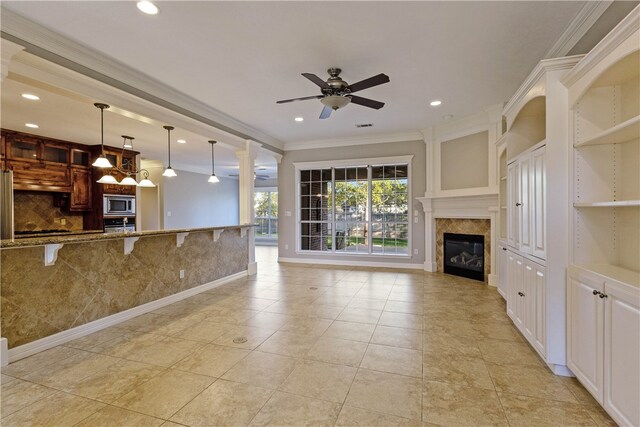 unfurnished living room featuring ceiling fan, ornamental molding, light tile patterned floors, and ornate columns