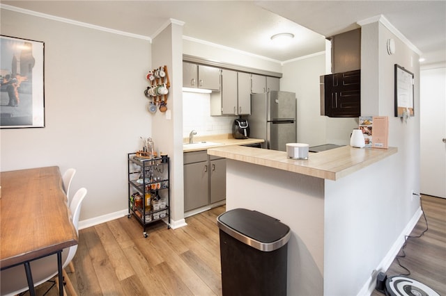 kitchen featuring gray cabinetry, ornamental molding, light countertops, and freestanding refrigerator