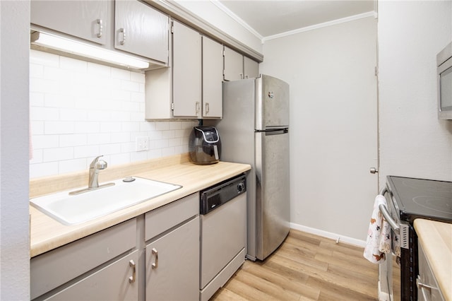 kitchen featuring light wood finished floors, backsplash, ornamental molding, appliances with stainless steel finishes, and a sink