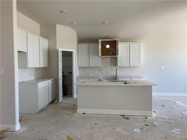 kitchen featuring white cabinets, decorative backsplash, a kitchen island with sink, and sink