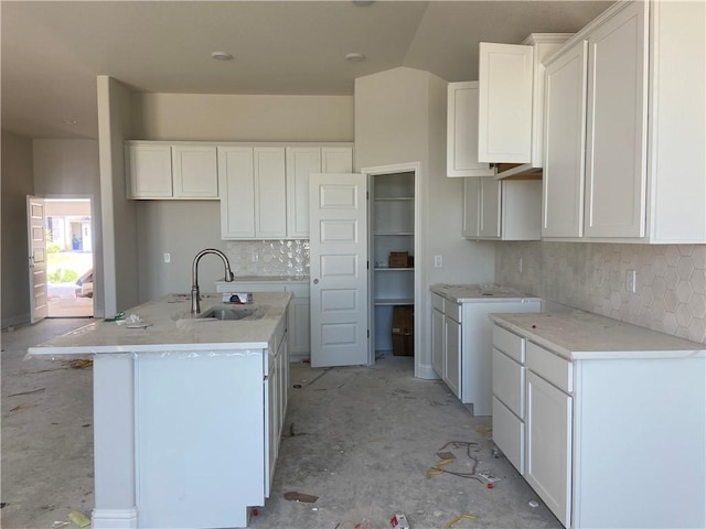 kitchen with decorative backsplash, a center island with sink, white cabinetry, and sink