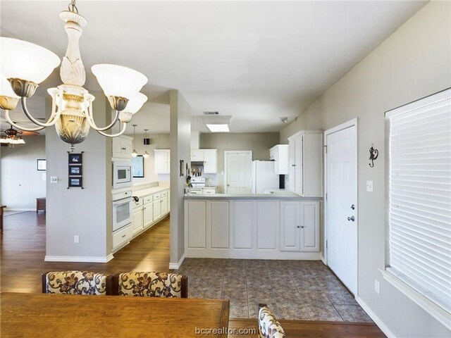 kitchen with kitchen peninsula, white cabinets, white appliances, and an inviting chandelier