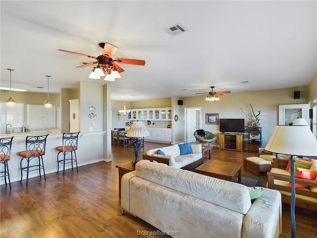 living room featuring dark hardwood / wood-style flooring, ceiling fan with notable chandelier, and sink