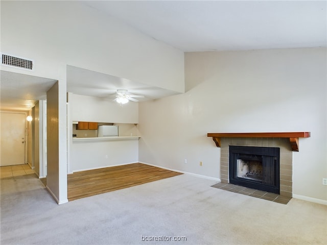 unfurnished living room featuring a tiled fireplace, light carpet, and ceiling fan