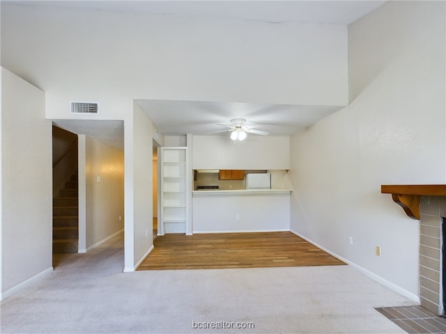 unfurnished living room with ceiling fan, a fireplace, and light carpet