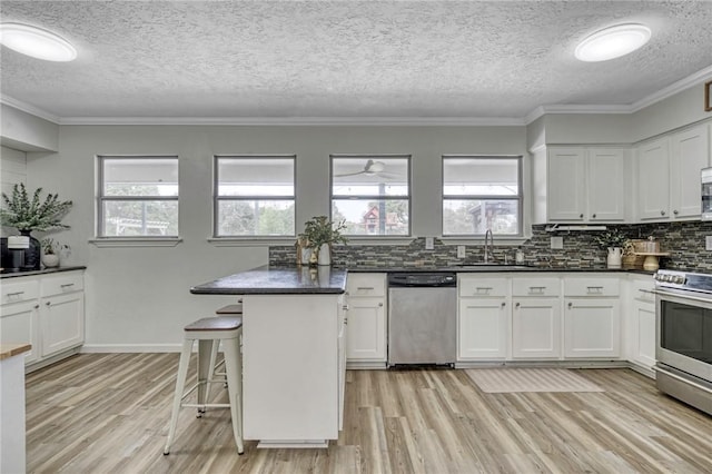 kitchen with a sink, stainless steel appliances, light wood finished floors, backsplash, and dark countertops