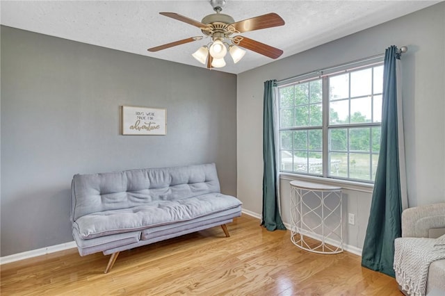living area with a textured ceiling, wood finished floors, baseboards, and ceiling fan