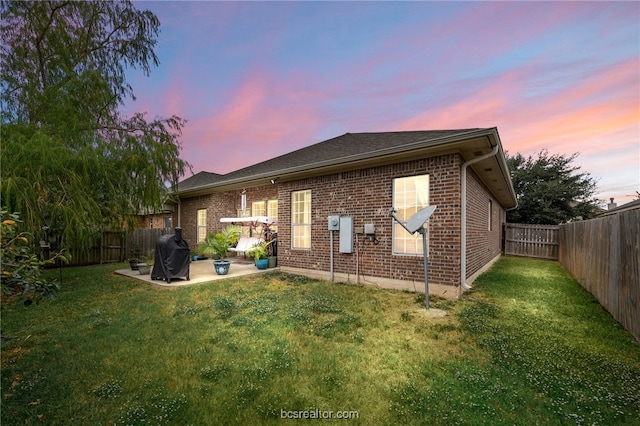 934 Dove Landing Ave, College Station, TX 77845 - back of house at dusk featuring a lawn, brick siding, a fenced backyard, and a patio area