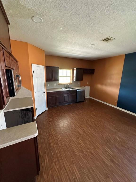 1113 W 10th St, Hearne, TX 77859 - kitchen with dishwasher, a textured ceiling, dark wood finished floors, light countertops, and dark brown cabinets