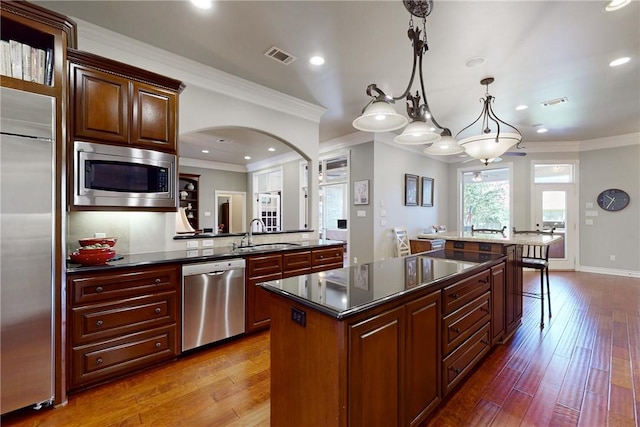 kitchen with sink, hardwood / wood-style flooring, hanging light fixtures, built in appliances, and a kitchen island