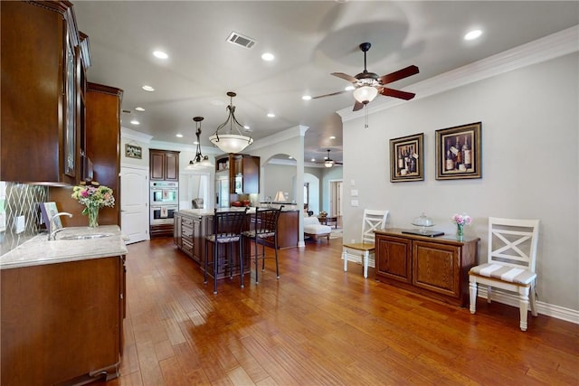 kitchen with sink, hanging light fixtures, dark hardwood / wood-style floors, double oven, and a kitchen island