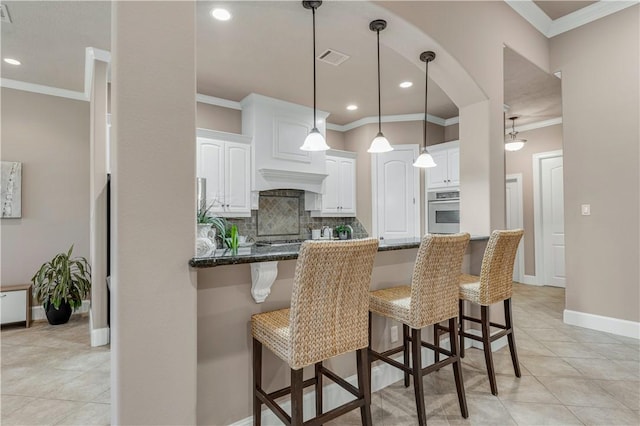 kitchen with backsplash, a breakfast bar, crown molding, white cabinets, and oven