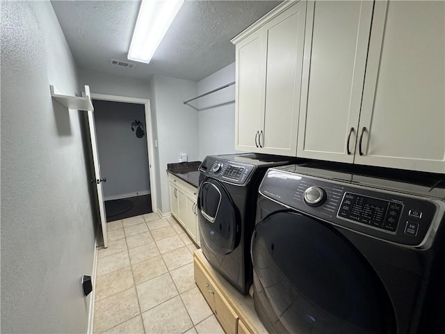 clothes washing area featuring light tile patterned floors, washer and clothes dryer, cabinets, and a textured ceiling