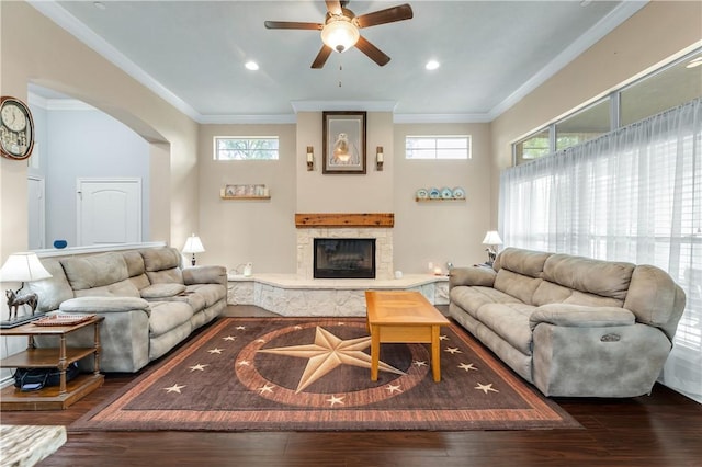 living room with crown molding, a stone fireplace, ceiling fan, and dark hardwood / wood-style flooring