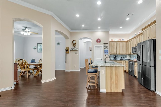 kitchen with light brown cabinetry, a breakfast bar area, stainless steel appliances, light stone countertops, and a center island with sink