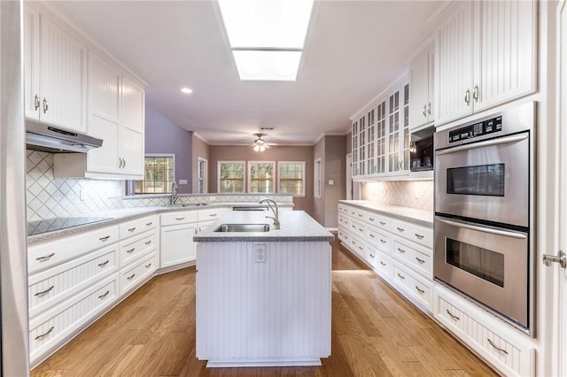 kitchen with stainless steel double oven, white cabinets, sink, a kitchen island with sink, and black electric cooktop