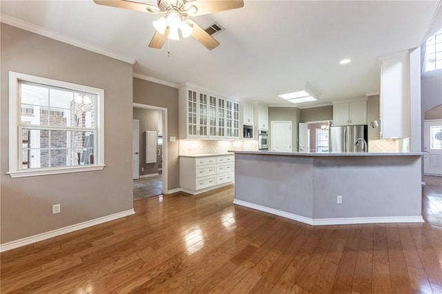 kitchen featuring decorative backsplash, wood-type flooring, white cabinets, and appliances with stainless steel finishes