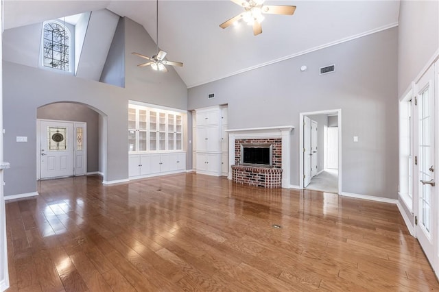 unfurnished living room with hardwood / wood-style floors, a brick fireplace, ceiling fan, a high ceiling, and a wealth of natural light