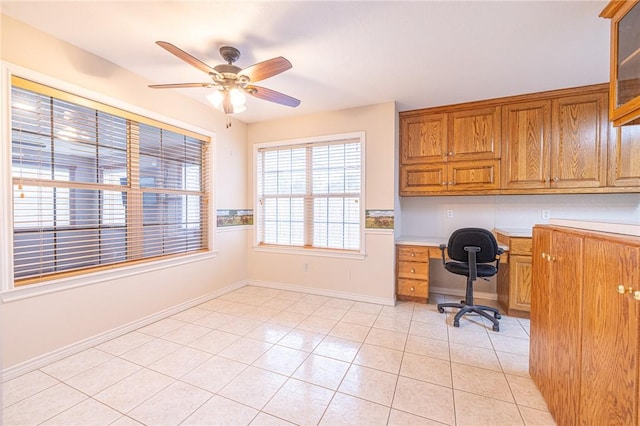 unfurnished office with built in desk, ceiling fan, and light tile patterned floors