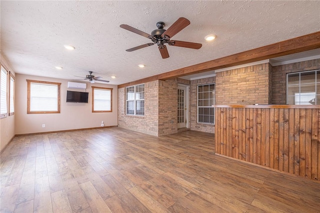 unfurnished room featuring brick wall, wood-type flooring, a textured ceiling, and a wall mounted air conditioner