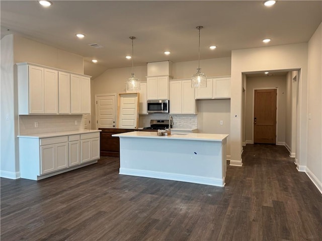 kitchen featuring white cabinetry, appliances with stainless steel finishes, a center island with sink, and decorative light fixtures