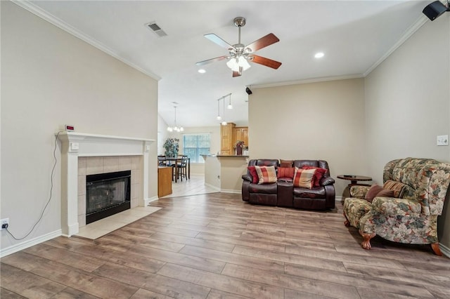 living room featuring a tile fireplace, ceiling fan with notable chandelier, light hardwood / wood-style floors, and ornamental molding