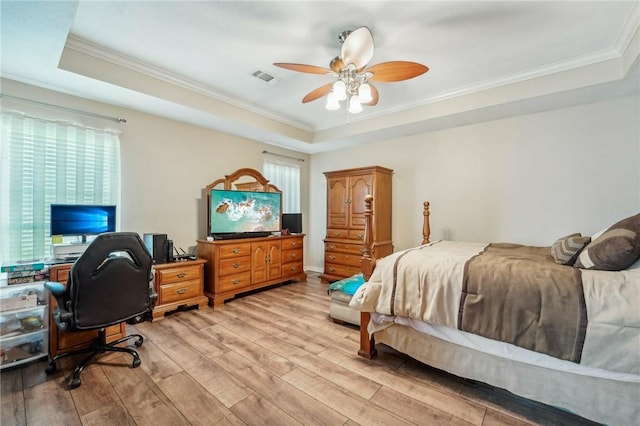 bedroom with ceiling fan, a raised ceiling, light wood-type flooring, and ornamental molding