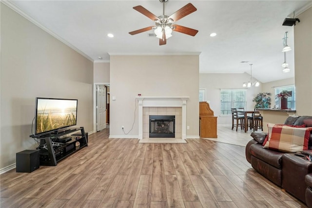 living room with light hardwood / wood-style flooring, crown molding, vaulted ceiling, a fireplace, and ceiling fan with notable chandelier