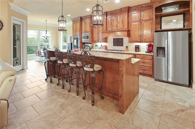 kitchen featuring appliances with stainless steel finishes, light stone countertops, an island with sink, and hanging light fixtures